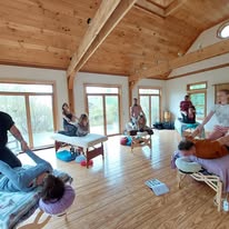 Group of therapists in training workshop with massage tables in a bright wood-paneled room
