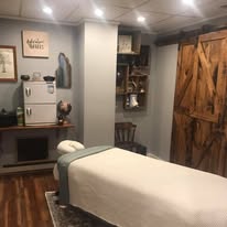 Wide angle of treatment room with rustic barn sliding doors, shelving, and massage table
