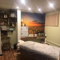 Treatment room with sunset-over-sunflower-field wall mural and massage table